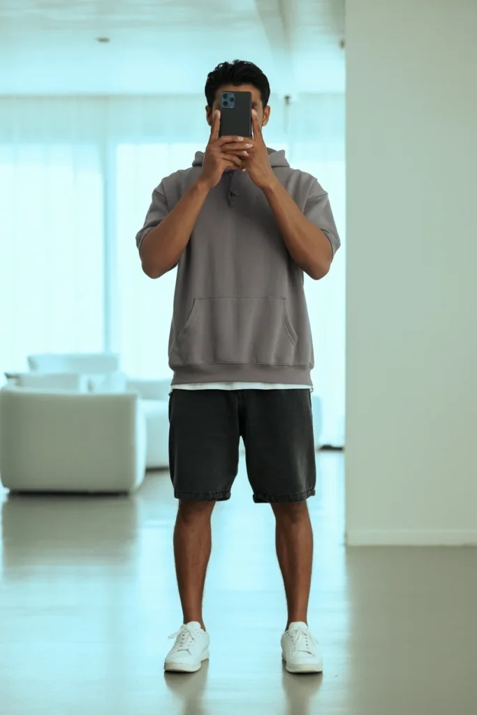 A man in a grey short-sleeve hoodie and black denim shorts, ideal Summer Streetwear Outfits for Men.