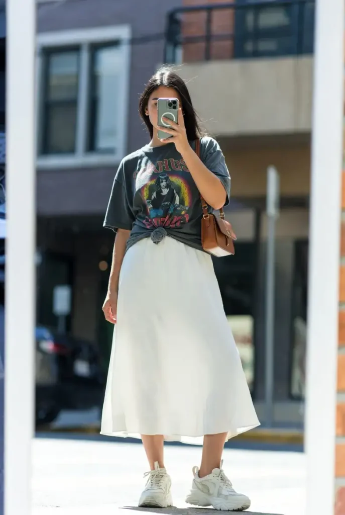 One of the 13 White Maxi Skirt Outfits: a knotted vintage graphic tee with a white maxi skirt and chunky white sneakers