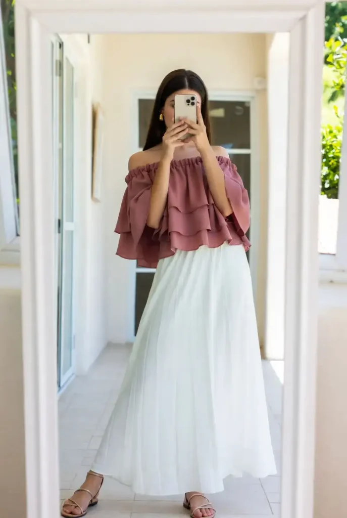 One of the 13 White Maxi Skirt Outfits: a dusty rose off-the-shoulder ruffled top with a flowy white maxi skirt and sandals.