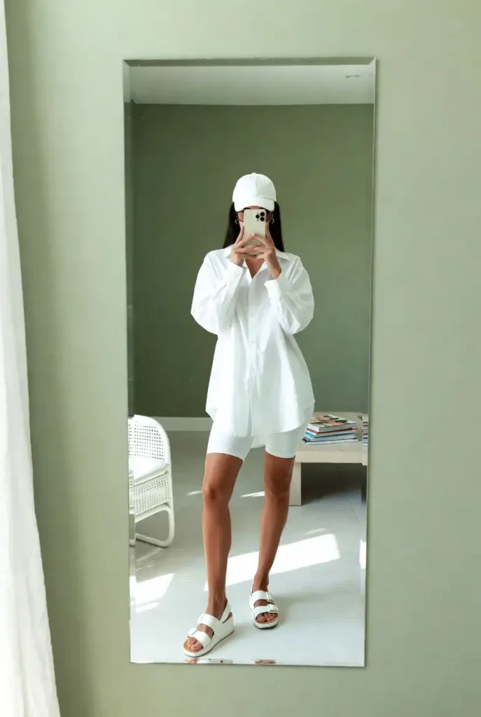 White oversized shirt dress over bike shorts mirror selfie from 10 All White Outfit Ideas for Spring
