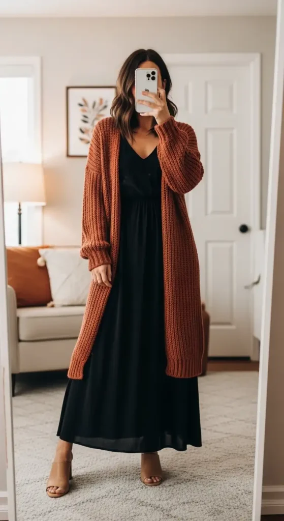 Black maxi dress casual outfit idea layered with a chunky rust cardigan and nude mule heels — cozy mirror selfie