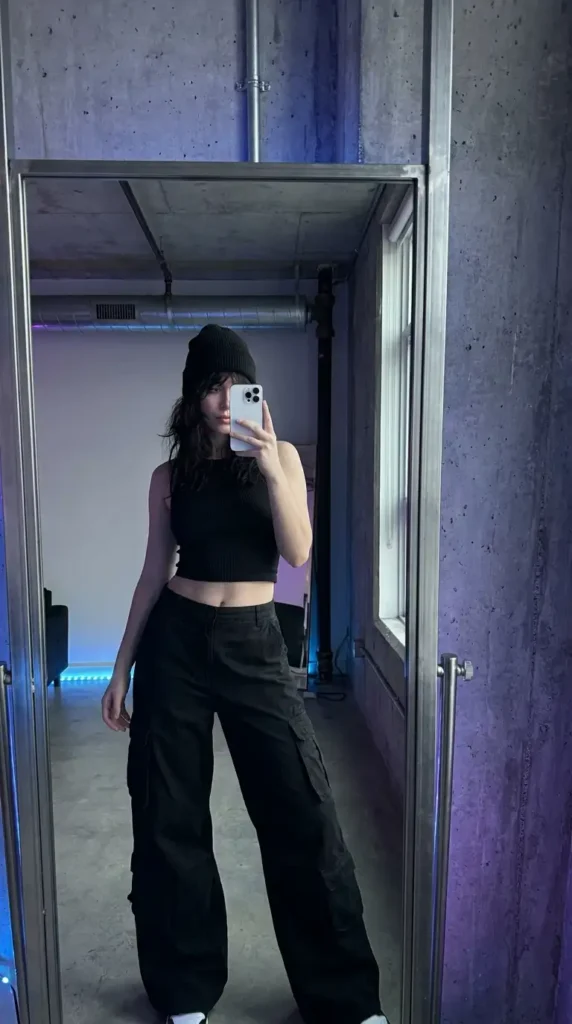 Black concert outfit ideas for women: ribbed crop top, wide-leg cargo pants, and black beanie, mirror selfie