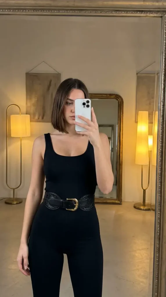 Black concert outfit ideas for women: sleek black jumpsuit cinched with a wide western leather belt, mirror selfie