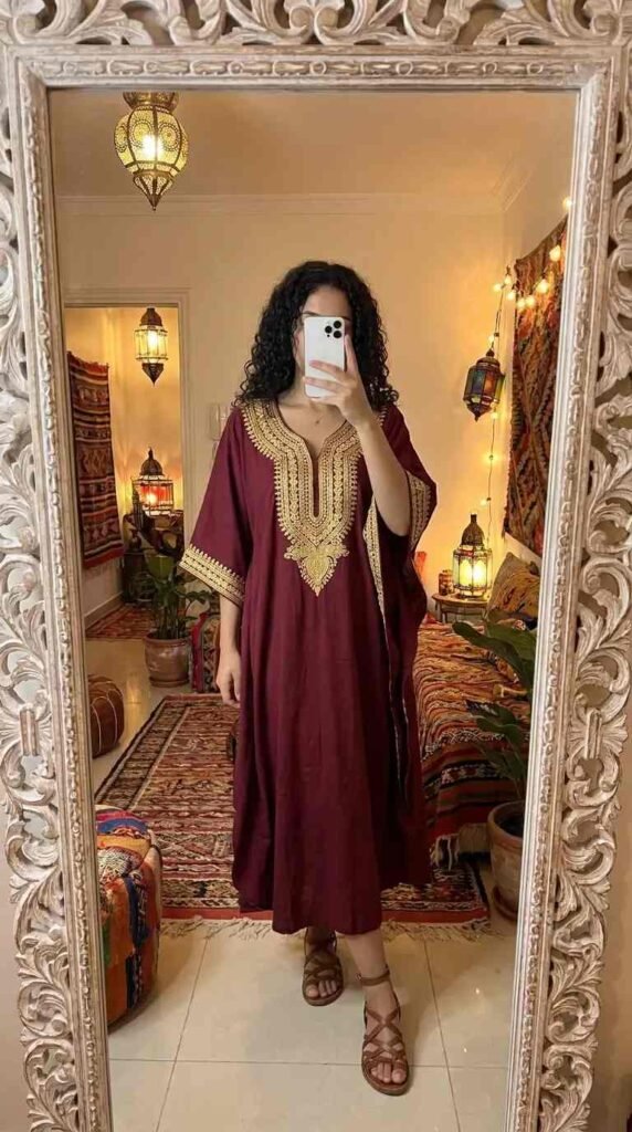 Dreamy 70s Boho Outfit Ideas: burgundy kaftan with gold embroidery, worn with strappy sandals in a Moroccan-inspired room.
