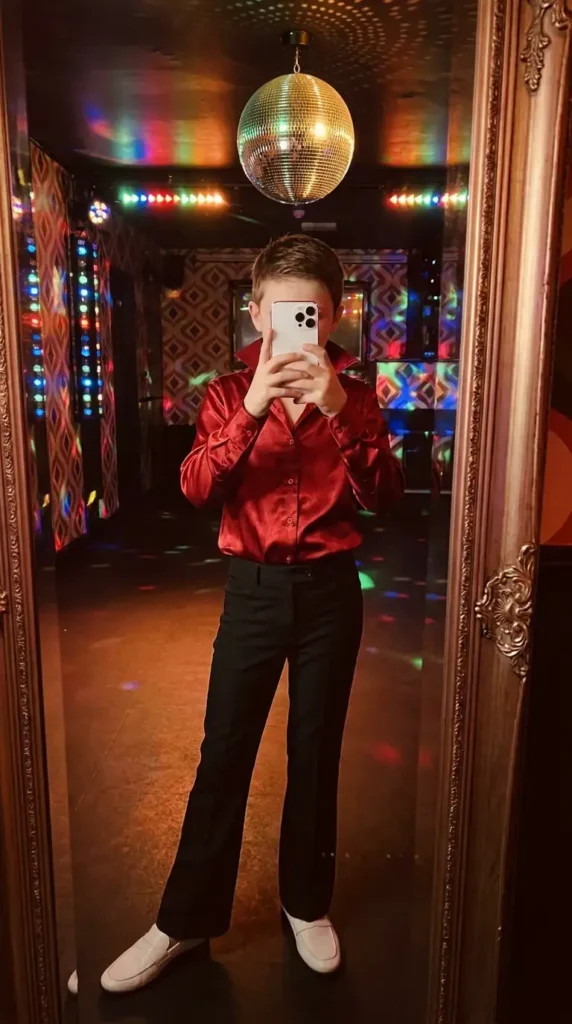 70s Outfit Ideas for Boys: disco-ready red satin button-up shirt with black flared trousers and white loafers under a mirror ball.