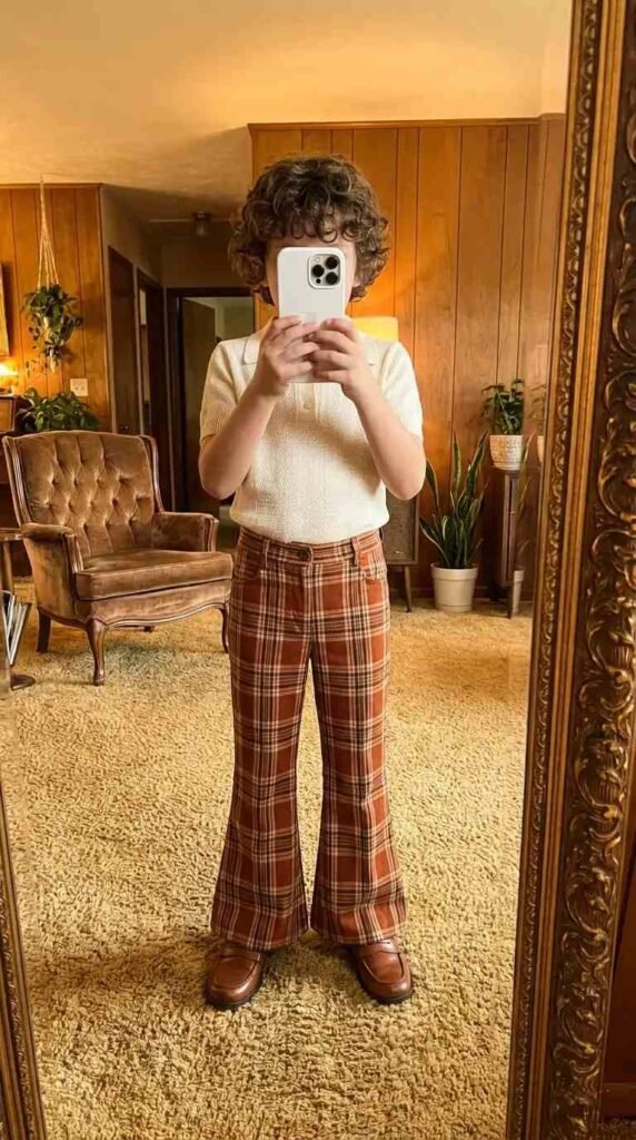 70s Outfit Ideas for Boys: cream polo shirt styled with rust plaid bell-bottom trousers and brown leather loafers in retro room.