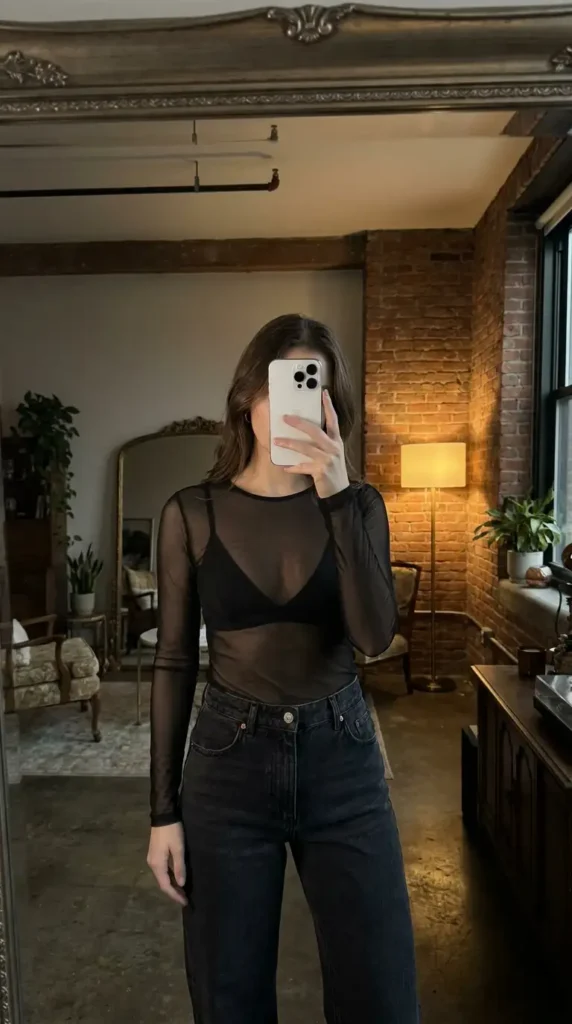 Black concert outfit ideas for women: sheer long-sleeve mesh top over black bralette with dark high-waisted jeans