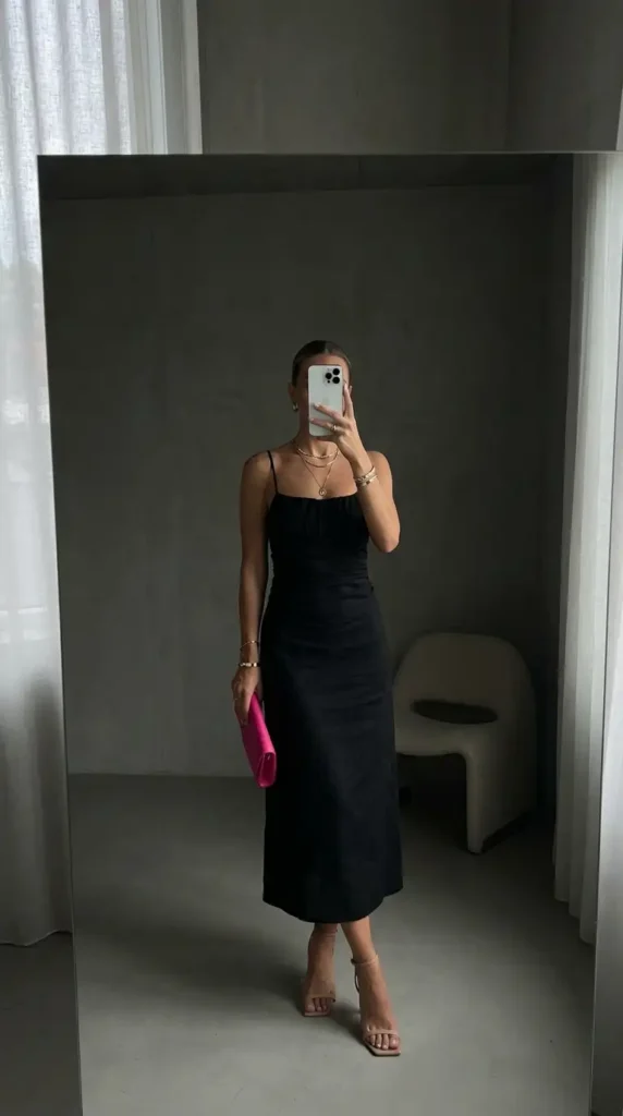 Wedding guest outfit ideas: sleek black linen midi slip dress with gold jewelry and pink clutch