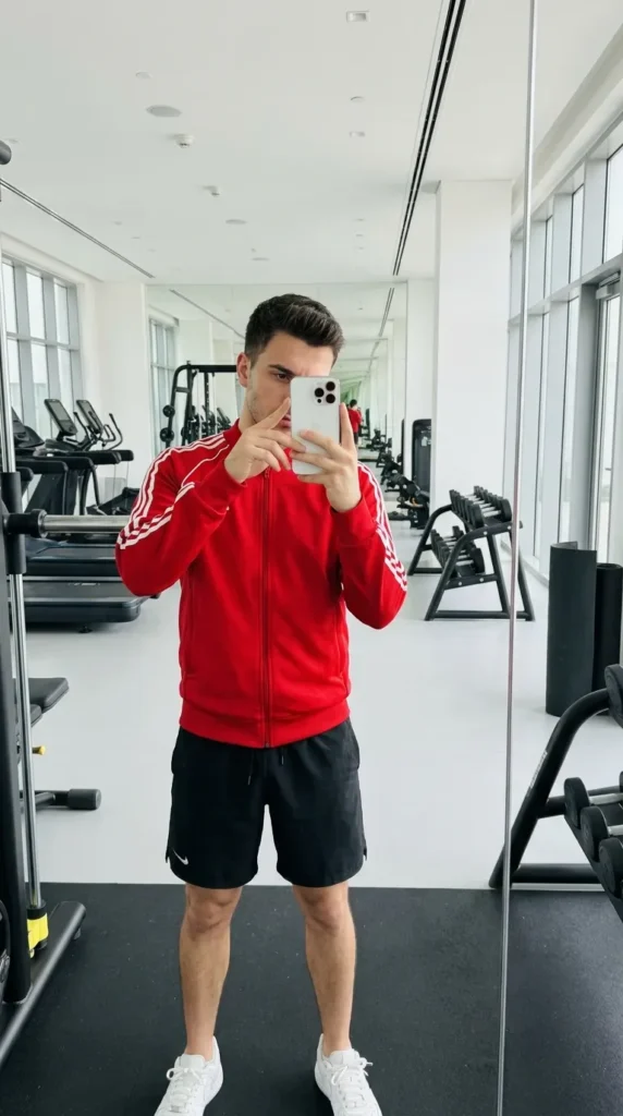 Man in red track jacket and black shorts gym mirror selfie from 20 Red Outfit Ideas for Men That Actually Slay