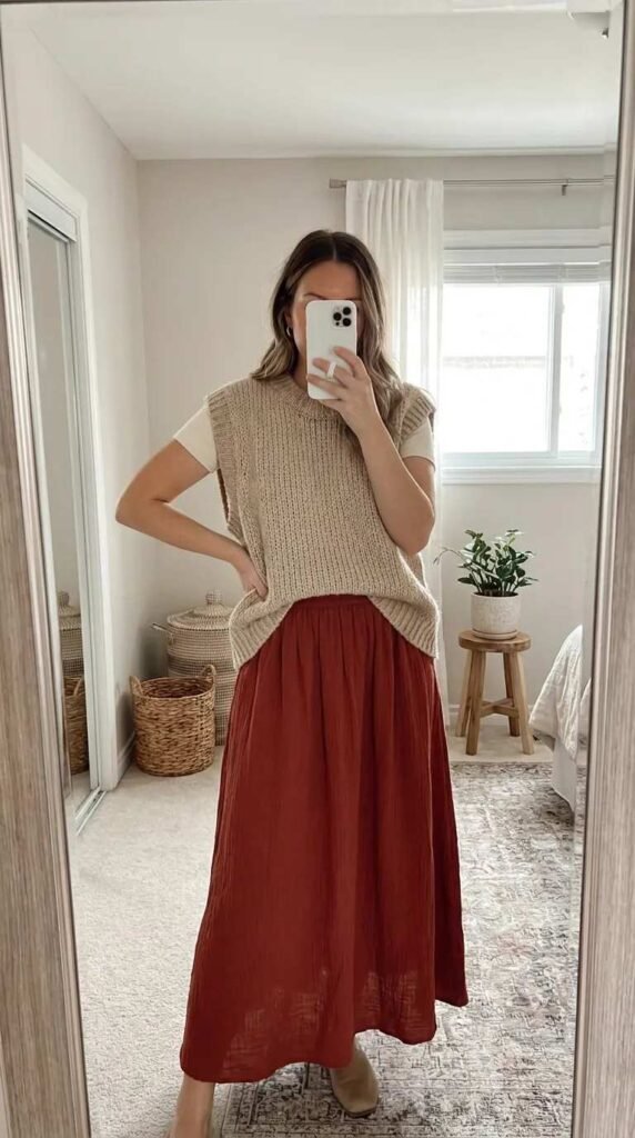 Woman wearing oversized knit vest and long red skirt outfit ideas for this summer in a cozy space.